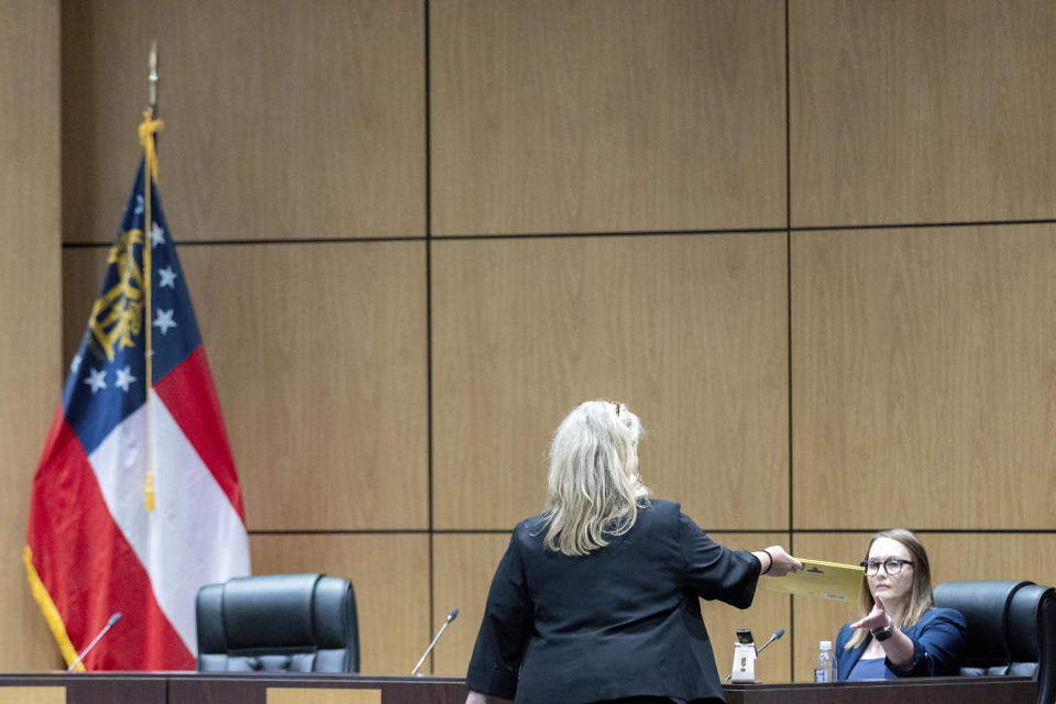 Sherry Culves, an attorney representing the Cobb County School District, hands teacher Katie Rinderle the book "My Shadow is Purple" during a hearing at the Cobb County Board of Education in Marietta, Ga, Thursday, Aug. 10, 2023. Rinderle is facing termination after reading "My Shadow is Purple," a book about gender identity, to fifth graders. (Arvin Temkar/Atlanta Journal-Constitution via AP)