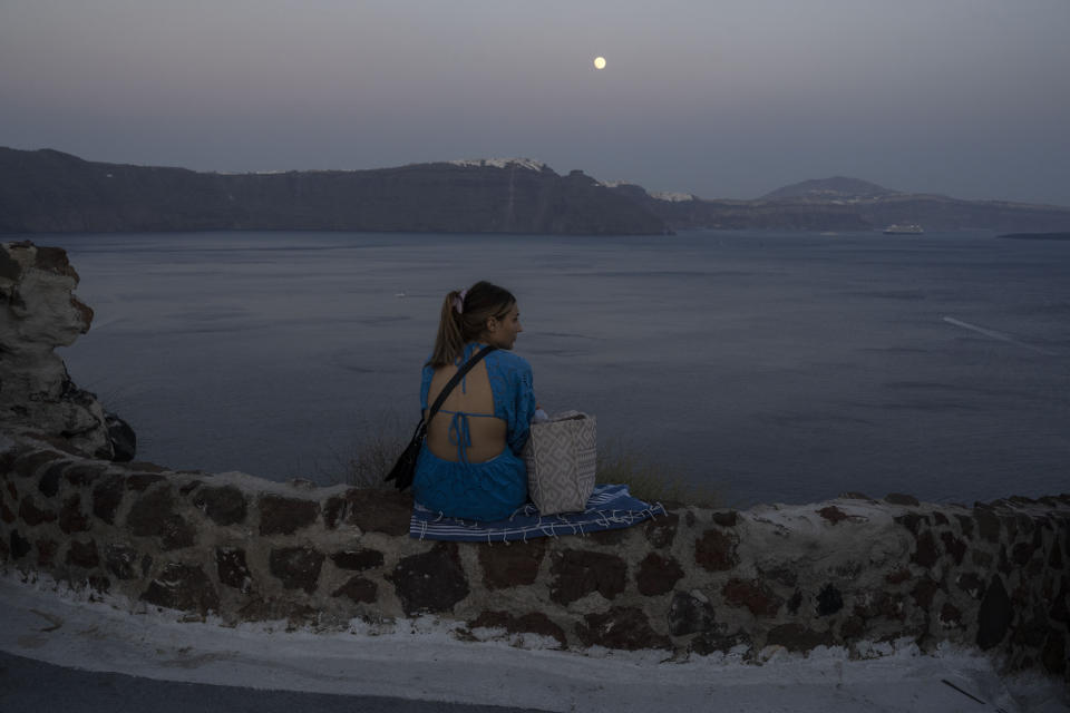 A woman looks on the Aegean Sea as the moon rises in Santorini island, Greece, on Monday, June 13, 2022. (AP Photo/Petros Giannakouris)