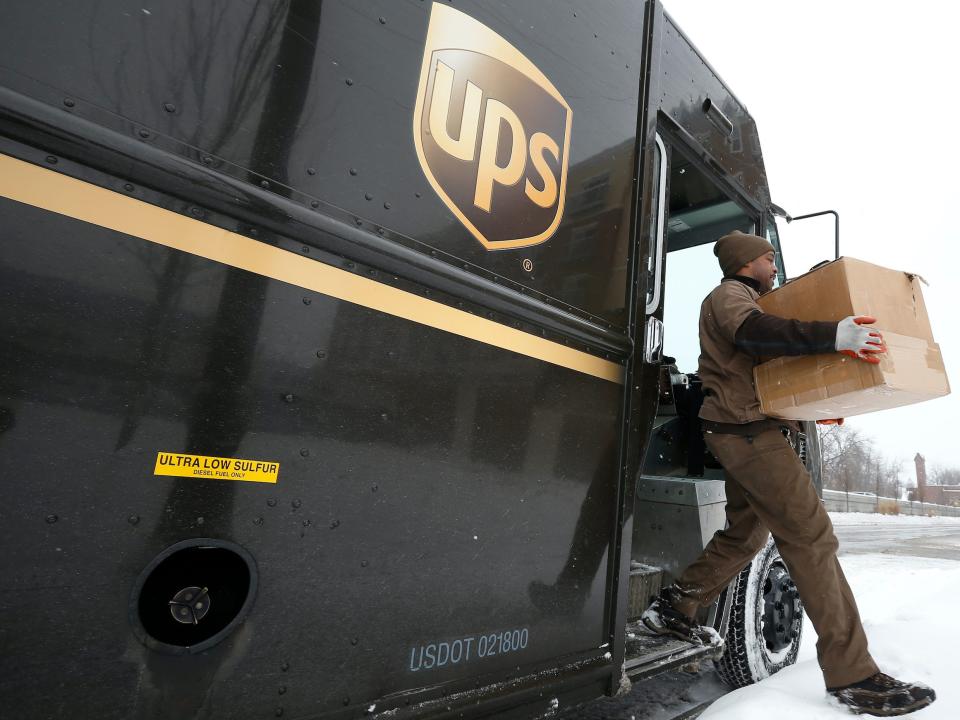 A UPS driver unloading a large cardboard box from a van.