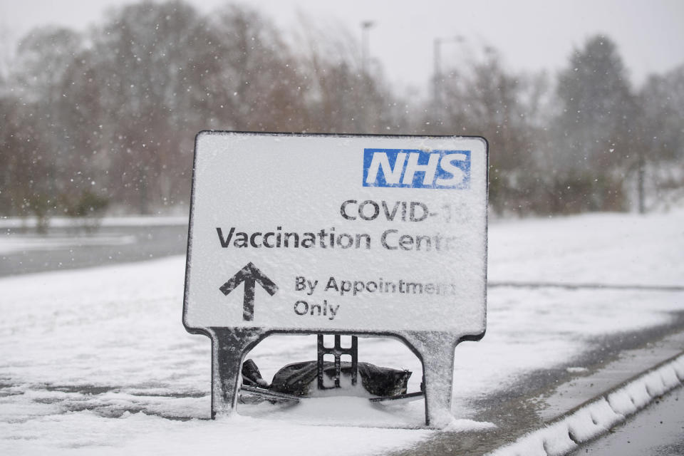 A snow covered sign directs people to the Covid-19 vaccination centre at the Jobserve Community Stadium in Colchester, England, Sunday Feb. 7, 2021. The vaccination centre has been forced to close due to the bad weather, with heavy snow and bitterly cold winds set to bring widespread disruption to much of England. (Joe Giddens/PA via AP)