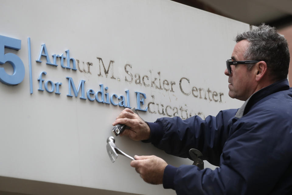 Worker Gabe Ryan removes a sign that includes the name Arthur M. Sackler at an entrance to Tufts School of Medicine, Thursday, Dec. 5, 2019, in Boston. Tufts University says it is stripping the Sackler name from its campus in recognition of the family's connection to the opioid crisis. (AP Photo/Steven Senne)