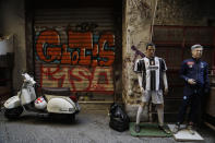 A vespa scooter is parked near statuettes of Juventus' Cristiano Ronaldo, left, and Napoli coach Carlo Ancelotti in downtown Naples, Italy Wednesday, Sept. 18, 2019. “One of the first figurines we made was of Diego Armando Maradona and you can imagine how many we sold. Still today, it sells a lot,” said craftsman Marco Ferrigno, who runs the most prominent shop on Via San Gregorio Armeno street, although while he doesn’t like to admit it, the player whose figurine Ferrigno sells the most these days is that of Cristiano Ronaldo. (AP Photo/Gregorio Borgia)