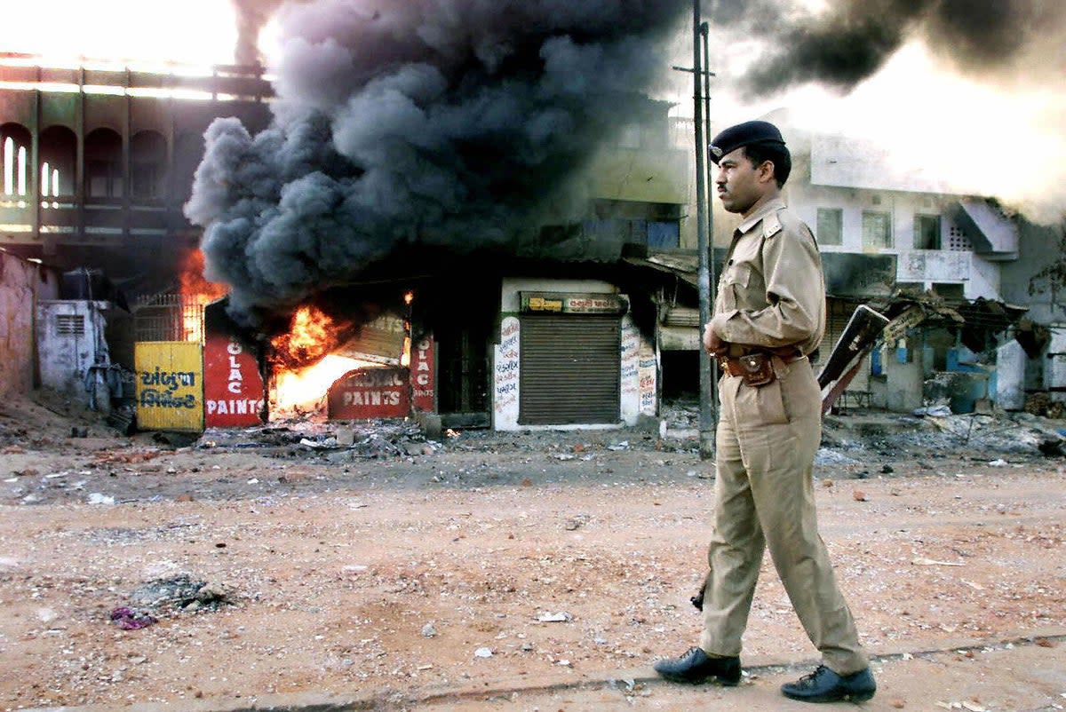 In this picture taken on 1 March 2002, an Indian policeman looks on as a row of shops burn during the Gujarat riots  (AFP via Getty Images)