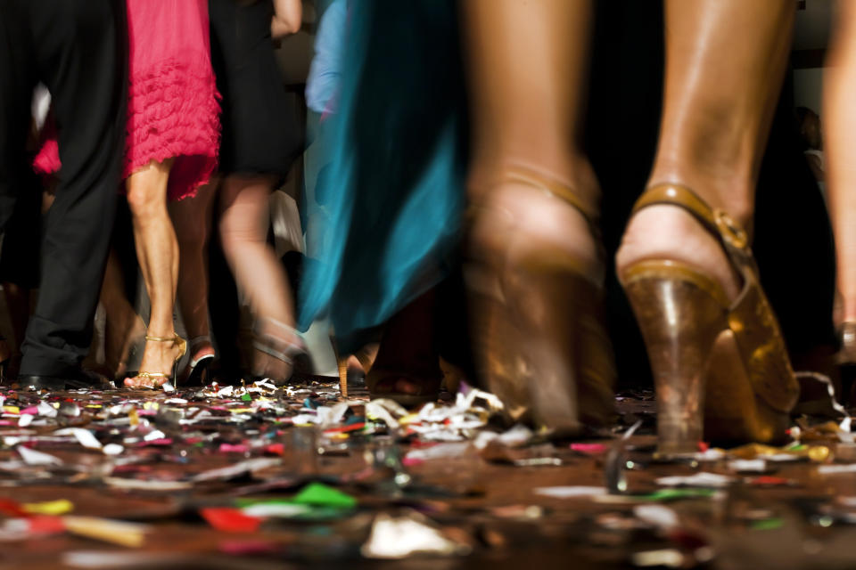 People's legs and feet in fancy shoes walking on a floor covered in confetti. Dresses and skirts are visible