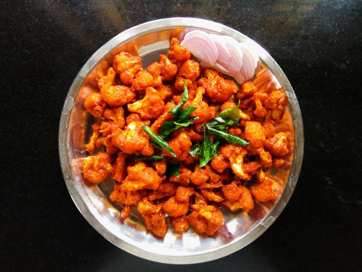 indian style cauliflower fry with sliced onion garnish with fry curry leaves