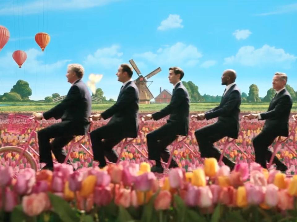 Men in suits riding a bike in flowers in Barbie