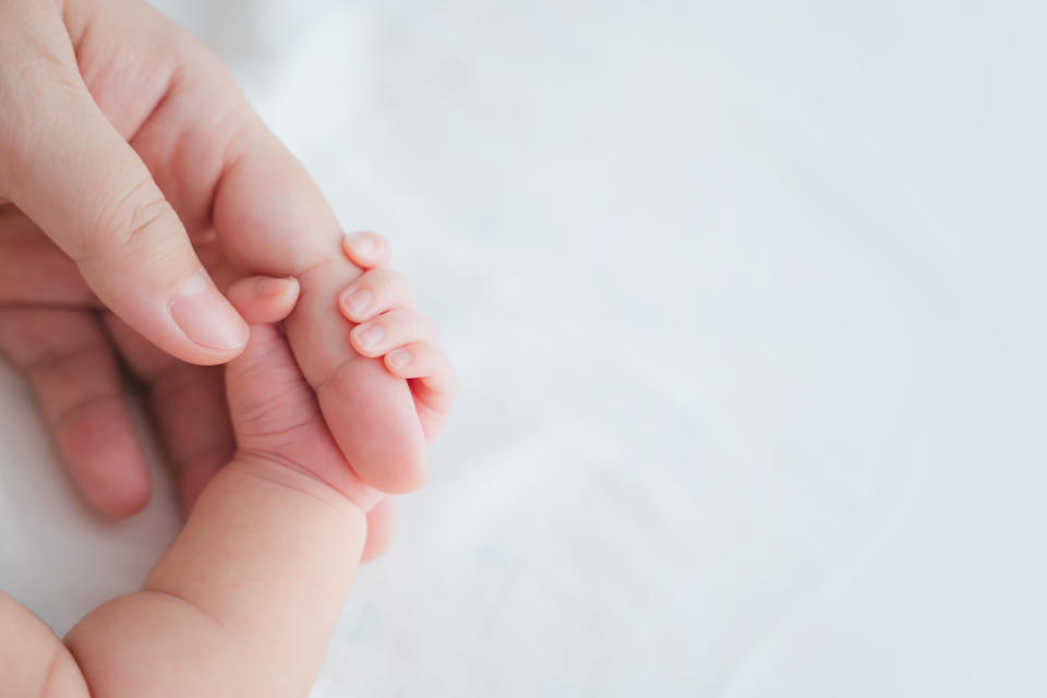 Mother uses her hand to hold her baby's tiny hand to make him feeling her love, warm and secure. Newborn.