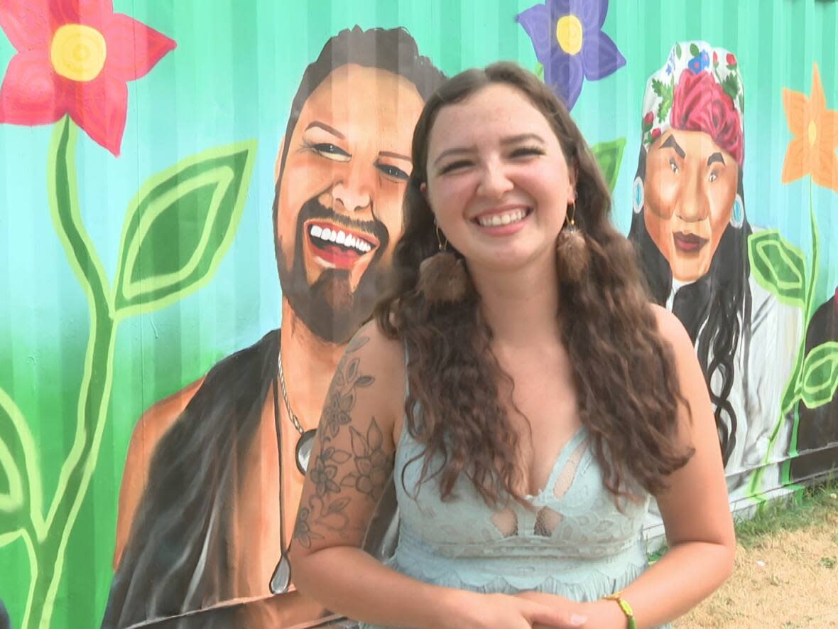 Bellerose stands in front of her mural, which includes 12 portraits of locals who identify as two-spirit or Indigiqueer. (Terri Trembath/CBC - image credit)