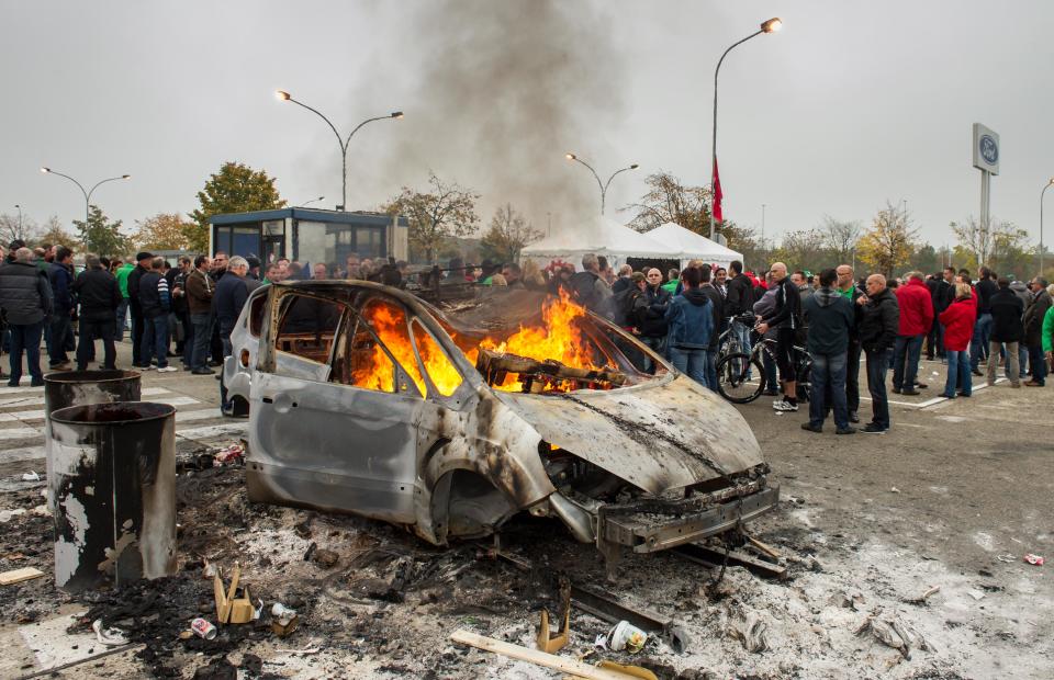 A car burns as workers block the main gate of the Ford plant in Genk, Belgium on Thursday Oct. 25, 2012. Ford Motor Co. announced Wednesday it planned to close a car plant in eastern Belgium — one of its main European factories — by the end of 2014, a move that would result in 4,500 direct job losses and 5,000 more among subcontractors. (AP Photo/Geert Vanden Wijngaert)