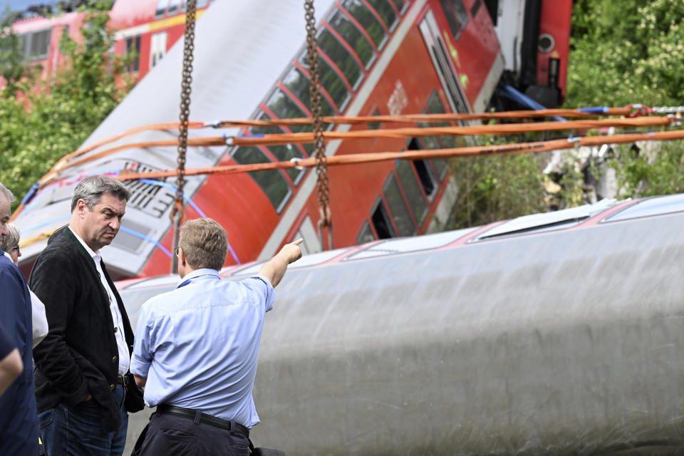 Bavarian Prime Minister Markus Soeder, left, visits the site of a train crash in Burgrain, near Garmisch-Partenkirchen, Germany, Saturday, June 4, 2022. Authorities say a train accident in the Alps in southern Germany on Friday left at least four people dead and many more injured. Police said the regional train headed for Munich appears to have derailed shortly after noon in Burgrain — just outside the resort town of Garmisch-Partenkirchen, from where it had set off. Three of the double-deck carriages overturned at least partly, and people were pulled out of the windows to safety. (Angelika Warmuth/dpa via AP)