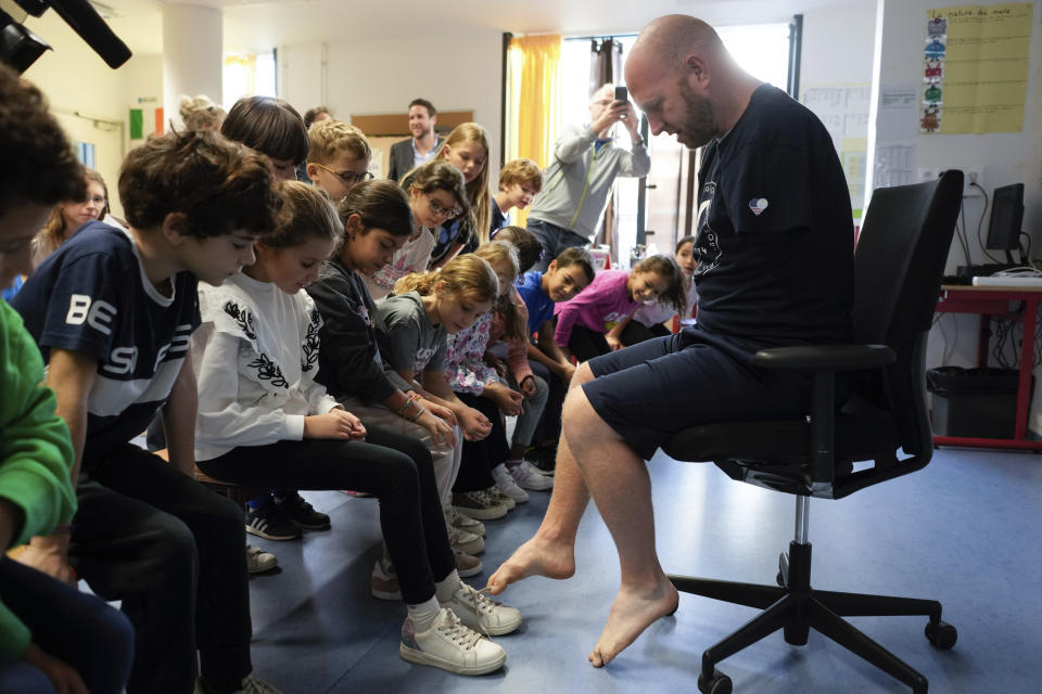 Archer Matt Stutzman of United States ties the shoes of a pupil with his foot, in a Paris school, in Paris, Wednesday, Oct. 4, 2023. Visiting France's capital before Paralympic tickets go on sale next week, Stutzman dropped by a Paris school on Wednesday and wowed its young pupils with his shooting skills. (AP Photo/Thibault Camus)