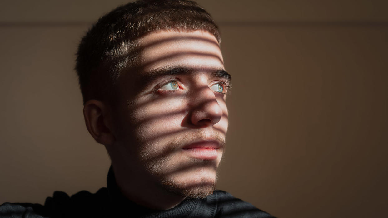  Close-up of thoughtful man sitting in shadows from blinds. 