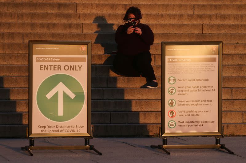 A woman in a mask takes a picture of the sunrise from the steps at the Lincoln Memorial during the coronavirus disease (COVID-19) outbreak, where normally thousands of Christians would gather for worship at Easter sunrise, in Washington