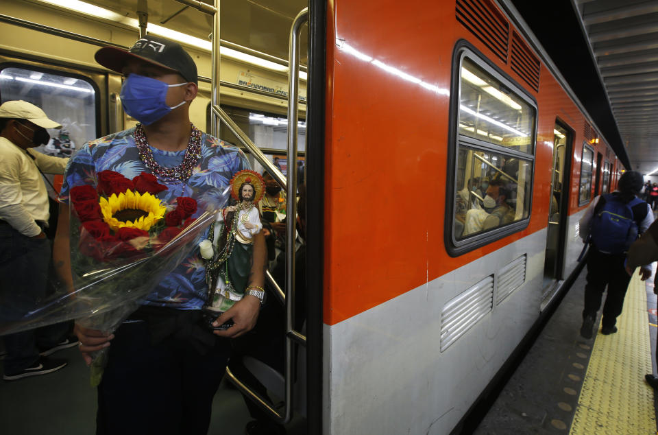 A devotee travels on the subway with his Saint Jude statue during the annual pilgrimage honoring Jude, the patron saint of lost causes, in Mexico City, Wednesday, Oct. 28, 2020. Thousands of Mexicans did not miss this year to mark St. Jude's feast day, but the pandemic caused Masses to be canceled and the rivers of people of other years outside the San Hipolito Catholic church were replaced by orderly lines of masked worshipers waiting their turn for a blessing. (AP Photo/Marco Ugarte)