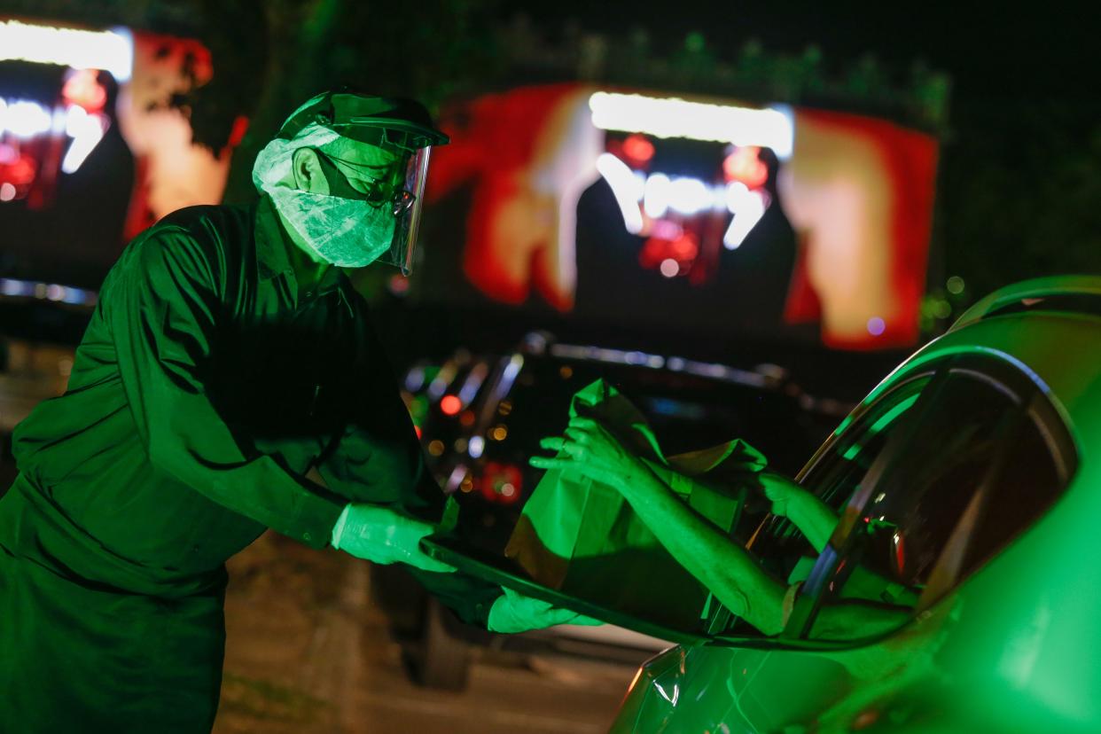 An employee wearing a face masks delivers food directly to the customer car during a drive-in movie screening of "Pulp Fiction" amidst the coronavirus (COVID-19) pandemic at Cine Lagoa Drive-in on July 19, 2020, in Rio de Janeiro, Brazil.