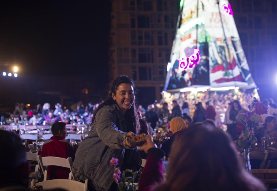 In this Monday, Dec. 23, 2019, photo, a volunteer serves food at a public Christmas dinner, as an initiative to help those in need, in Martyrs Square where anti-government activists are encamped in Beirut, Lebanon. Lebanon is entering its third month of protests, the economic pinch is hurting everyone, and the government is paralyzed. So people are resorting to what they've done in previous crises: They rely on each other, not the state. (AP Photo/Maya Alleruzzo)