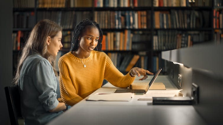 Two students looking at laptop in dark library