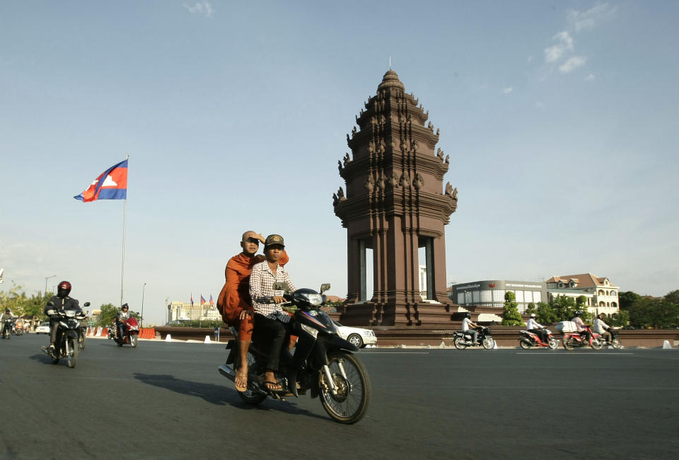 In this photo taken Feb. 25, 2013, a Cambodian motorists, transports a Buddhist monk, center, while driving past Independence Monument, in Phnom Penh, Cambodia. The Independence Monument is a striking shade of terra cotta by day and brightly illuminated by night. Glowing or not, it was constructed in 1958 to commemorate independence from the French that had been achieved five years prior. (AP Photo/Heng Sinith)