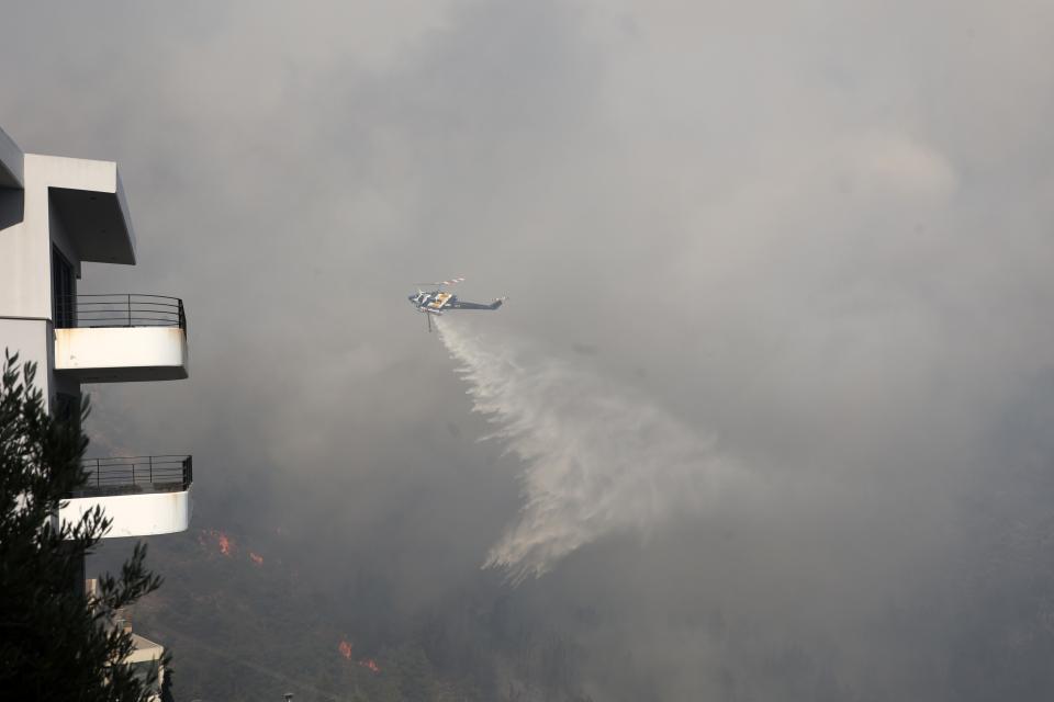 An helicopter drops water over a wildfire in Voula suburb, in southern Athens, Greece, Saturday, June 4, 2022. A combination of hot, dry weather and strong winds makes Greece vulnerable to wildfire outbreaks every summer. (AP Photo/Yorgos Karahalis)