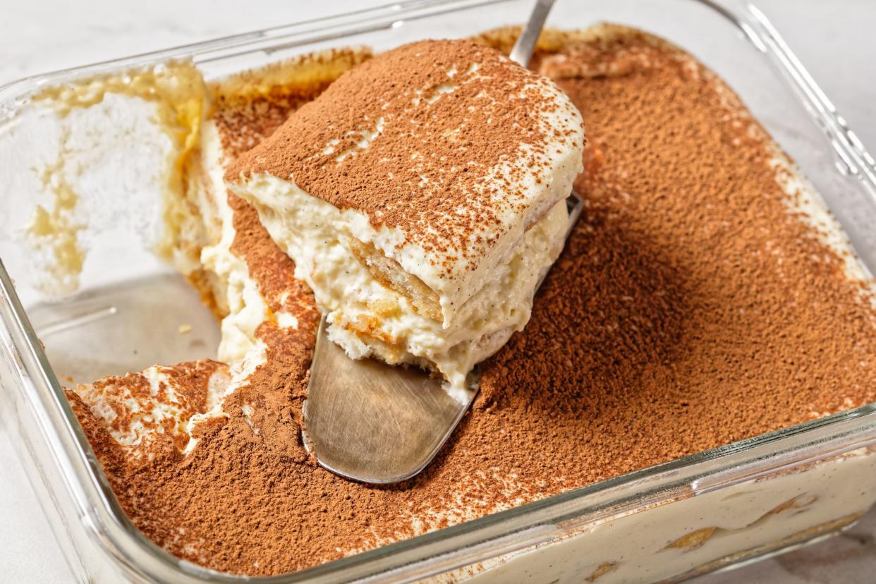 Italian dessert tiramisu of ladyfingers or savoiardi soaked in espresso and mascarpone cheese with egg whites served on a glass container on a white marble table, top view, close-up