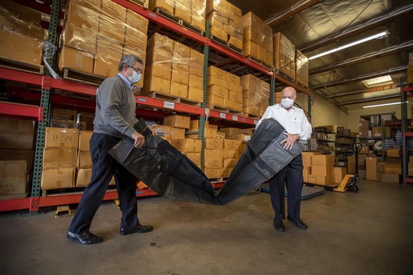 LAGUNA HILLS, CA - January 05: David Cameron, left, Executive Vice President, and Abdul Salam, president of Salam International, unpack a body bag in the warehouse. Salam International is a producer of body bags, morgue & mortuary supply equipment, precision instruments and pathology Tuesday, Jan. 5, 2021 in Laguna Hills, CA. (Allen J. Schaben / Los Angeles Times)