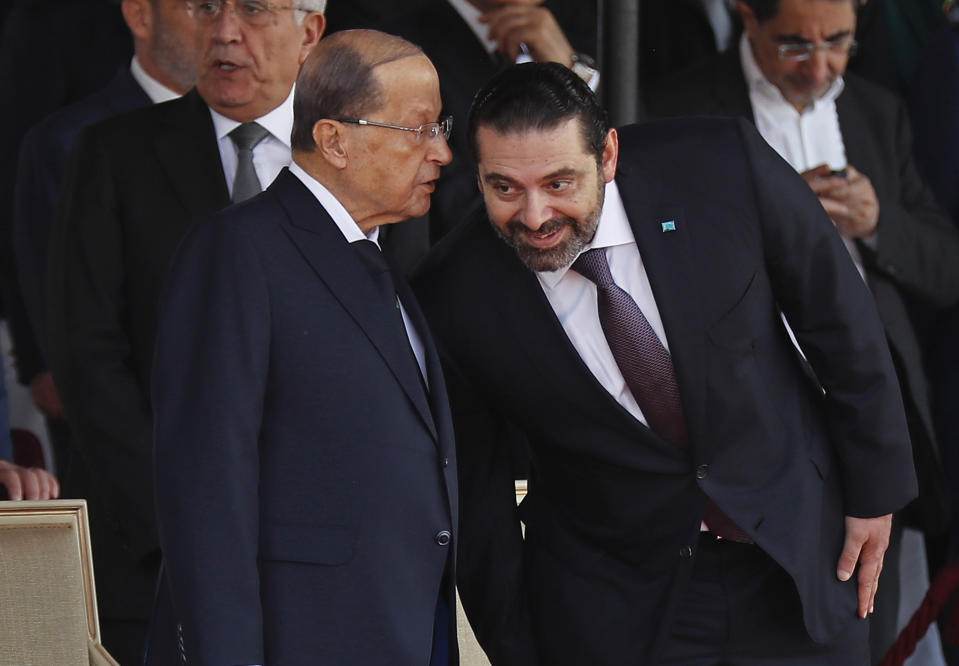 FILE - In this Nov. 22, 2018 file photo, Lebanese President Michel Aoun, left, whispers to Prime Minister Saad Hariri, during a military parade to mark the 75th anniversary of Lebanon's independence from France, in downtown Beirut, Lebanon. Lebanon's president called Wednesday, March 17, 2021 on the prime minister-designate to form a government immediately or step aside as the country plunges deeper into economic crisis. (AP Photo/Hussein Malla, File)