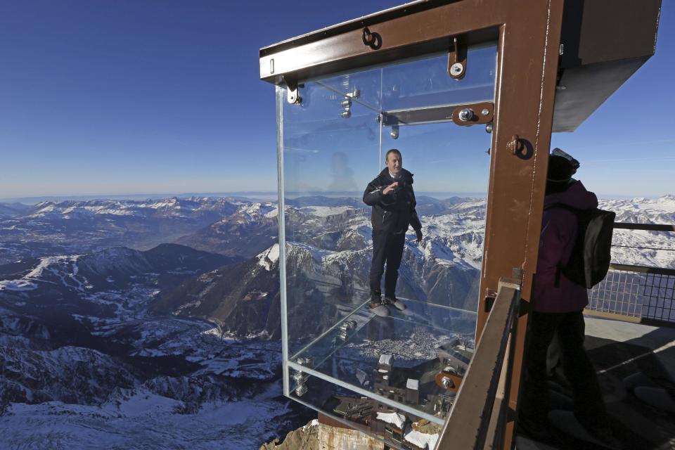 In this photo taken on Tuesday, Dec. 17, 2013, Mathieu Dechavanne, head of the Compagnie du Mont Blanc which runs the new attraction, stands in a glass cage named 'Pas dans le Vide' (Step into the Void) at the top of the Aiguille du Midi peak (3842-meters high or 12,604 feet), in the French Alps, during a press visit. Visitors can enjoy the view of Mont Blanc, Europe's highest mountain, from the platform. The attraction opens Saturday. (AP Photo/Alexis Moro)