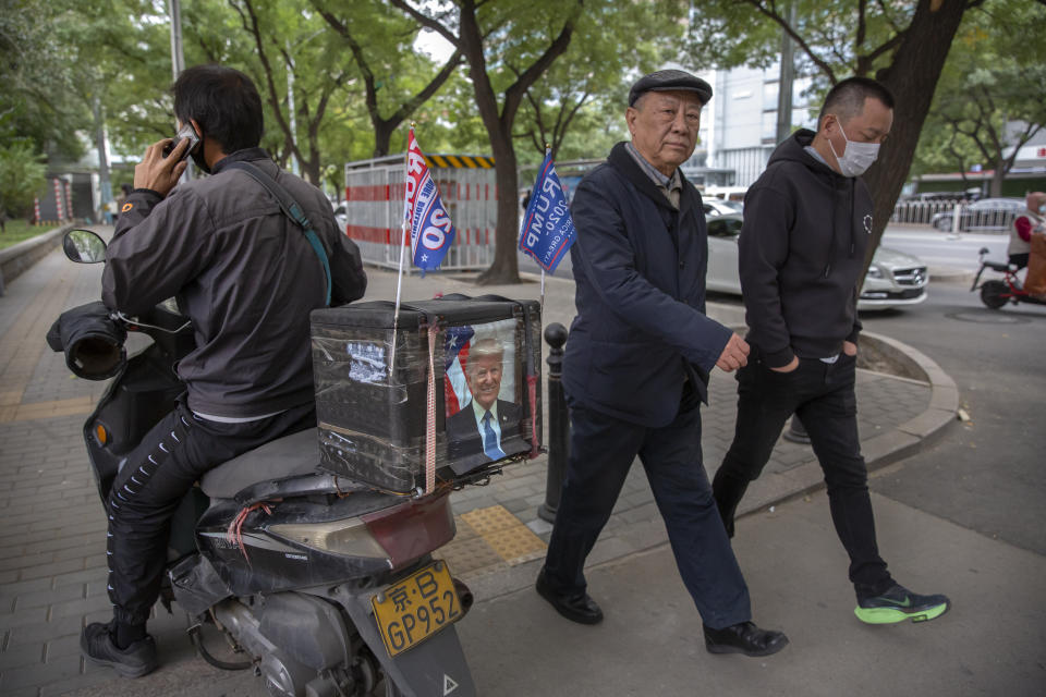 A delivery courier rides a motorbike decorated with a portrait of U.S. President Donald Trump and "Trump 2020" flags in Beijing, Wednesday, Oct. 14, 2020. Chinese leaders hope Washington will tone down conflicts over trade, technology and security if Joe Biden wins the Nov. 3 presidential election. But any shift is likely to be in style, not substance, as frustration with Beijing increases across the American political spectrum. (AP Photo/Mark Schiefelbein)