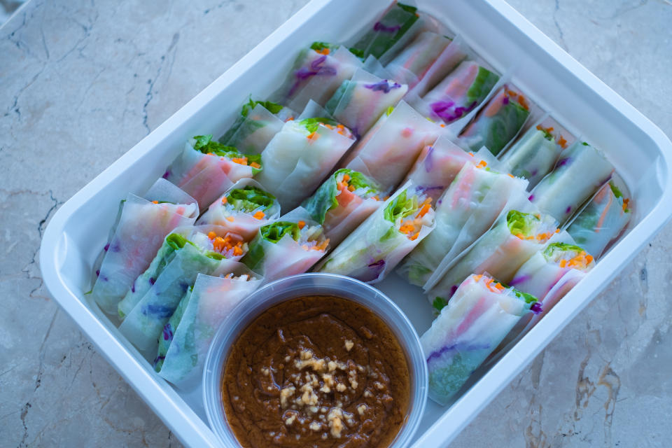 Twenty-five spring rolls and accompanying dip are in a white rectangular container