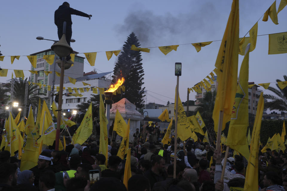 Palestinian Fatah supporters light a torch while others wave the movement's flags during a rally marking the 58th anniversary of Fatah movement foundation at the Unknown soldier square in Gaza City, Saturday, Dec. 31, 2022. Hundreds of thousands of Palestinians thronged a Gaza City park Saturday to mark the 58th founding anniversary of Fatah party, a rare show of popularity in the heartland of the militant Hamas group, Fatah's main rival. (AP Photo/Adel Hana)