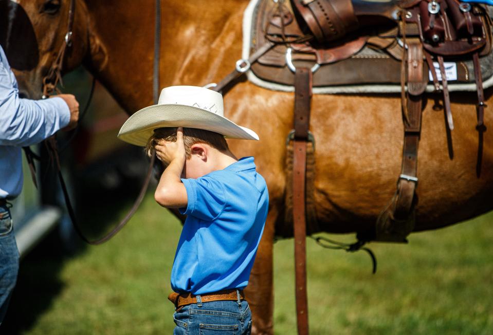 Beau Pennington (7) wipes sweat off of his forehead while his father, Trevor, saddles up their horse, Socks, at 1822 Farms in Williamsport, Tenn. on Monday, July 10, 2023. 