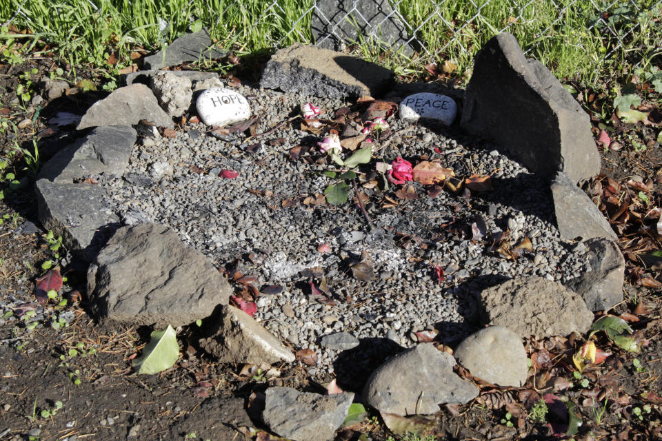 Two small stones that say "hope" and "peace" respectively and two flowers lay inside a circle of rocks on the ground in Portland, Ore., on Oct. 17, 2023. The rock circle is next to the site of a former homeless encampment that was cleared several times over the course of the year. With homelessness on the rise in the U.S. and a lack of affordable housing, cities and states are cracking down on mushrooming tent encampments. Cities across the U.S. are struggling with and cracking down on tent encampments as the number of homeless people grows, largely due to a lack of affordable housing. Homeless people and their advocates say sweeps are cruel and costly, and there aren't enough homes or beds for everyone. (AP Photo/Claire Rush)