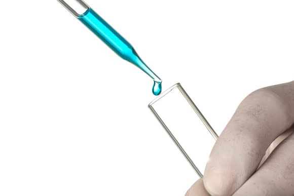 Pipette dropping a teal-colored liquid into a test tube.