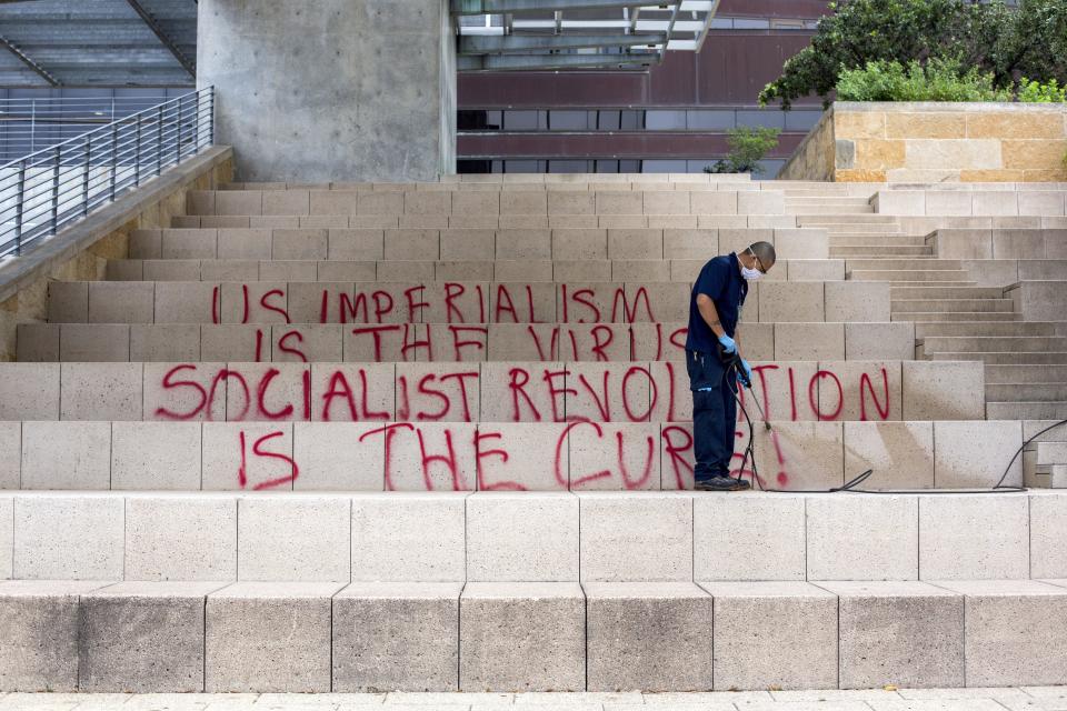 An employee attempts to wash off graffiti on the steps of City Hall in Austin, Texas, on Tuesday. Overnight, the building's front steps were vandalized with red paint and anti-capitalism graffiti messages as the state prepares to slowly reopen one of the world’s largest economies.