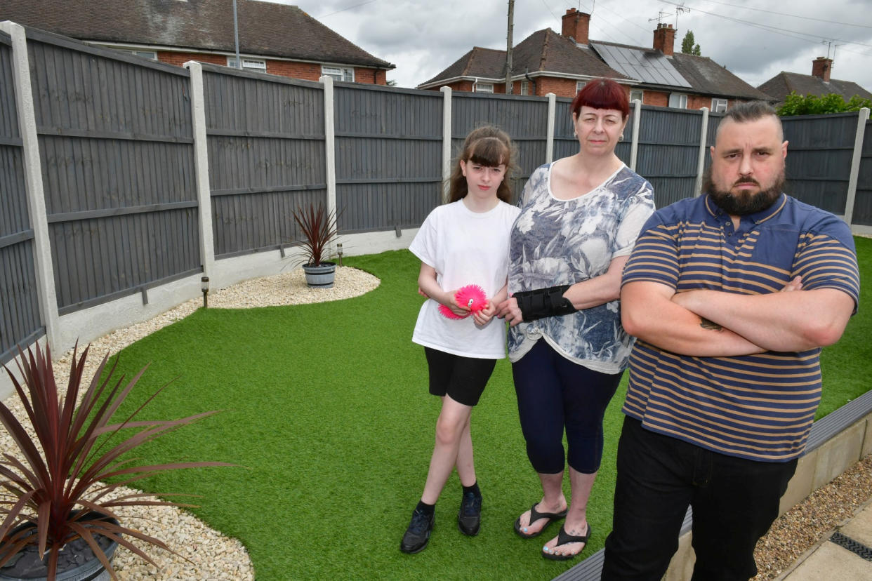 Cliff and Dawn Baker with daughter TJ, 10, of Edwinstowe, standing with their fence that the council has ordered to be romoved. See SWNS story SWLSfence. Parents have been ordered to remove a garden fence, which they claim helps keep their autistic daughter safe. Cliff Baker got permission from his landlord to put a 6ft fence in his garden in Edwinstowe 18 months ago, but did not realise he also needed planning approval from Newark and Sherwood District Council. He claims it is there to keep safe his ten-year-old daughter, TJ White, who has autism and is one of the only two people in the world with a rare chromosome depletion.