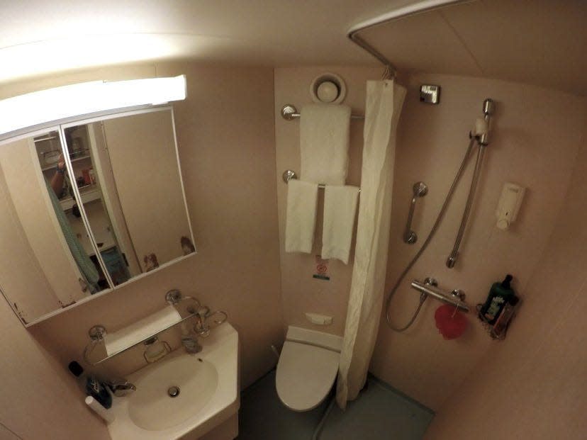 The crew bathroom on a cruise ship, which is very small with a tiolet, sink, and shower