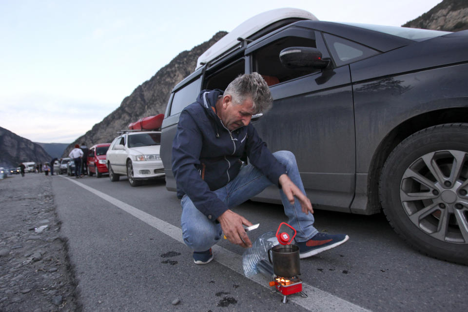 A man gets ready to cook next to his car, with other cars queuing to the border between Georgia and Russia at Verkhny Lars, as they leave Chmi, North Ossetia–Alania Republic, Russia, Wednesday, Sept. 28, 2022. Long lines of vehicles have formed at a border crossing between Russia's North Ossetia region and Georgia after Moscow announced a partial military mobilization. (AP Photo)