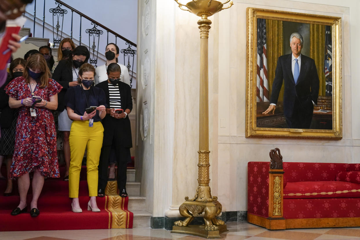 Attending to their cellphones, White House staff wait for the arrival of President Biden, next to a portrait of President Bill Clinton.