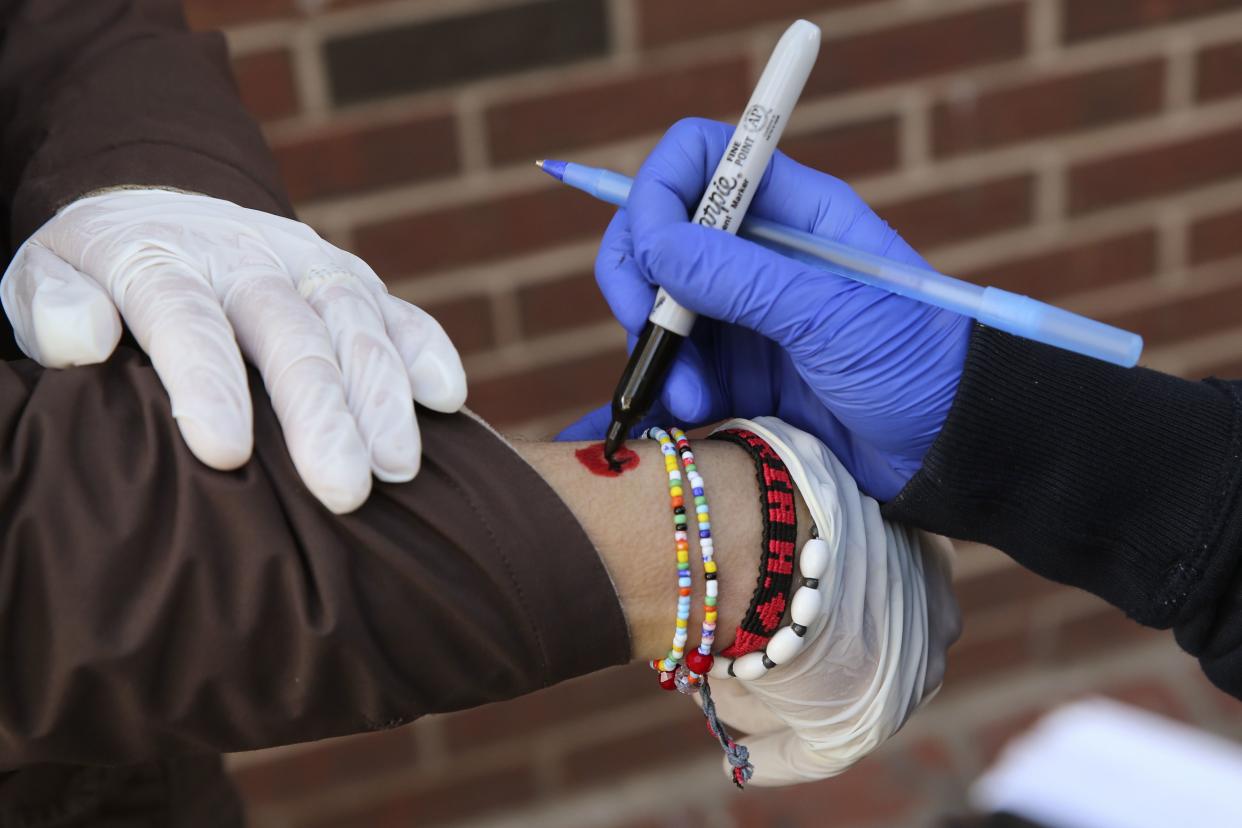 A woman has her wrist marked twice with a permanent marker while waiting with hundreds of people for food donations, given to those impacted by the COVID-19 virus outbreak, in Chelsea, Mass. on Tuesday, April 28, 2020.