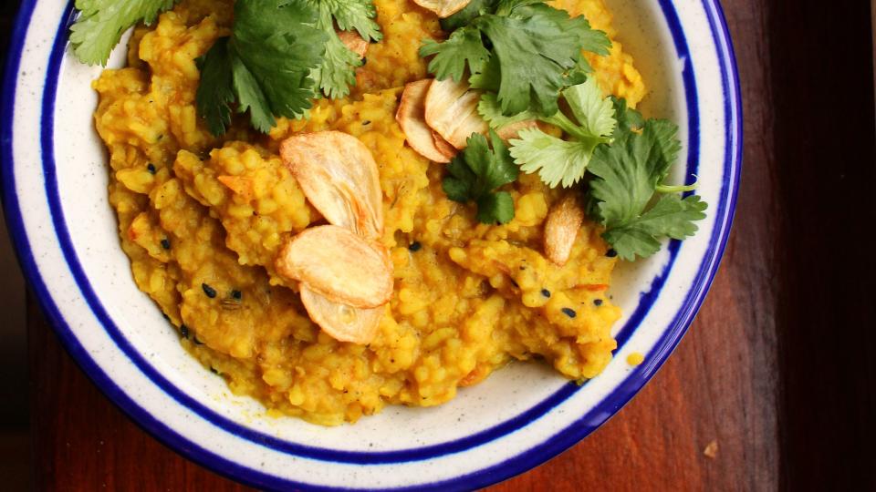 a bowl of turmeric yellow khichdi in a blue rimmed bowl with fried garlic chips and green cilantro