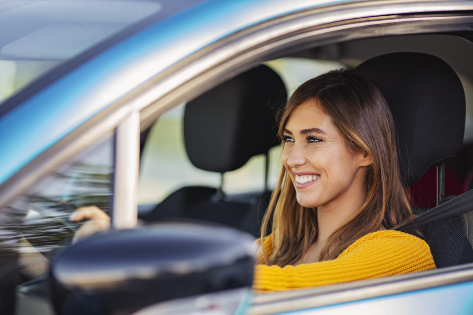 Young woman sitting in a car. Happy woman driving a car and smiling. Portrait of happy female driver steering car with safety belt. Cute young lady happy driving car.
