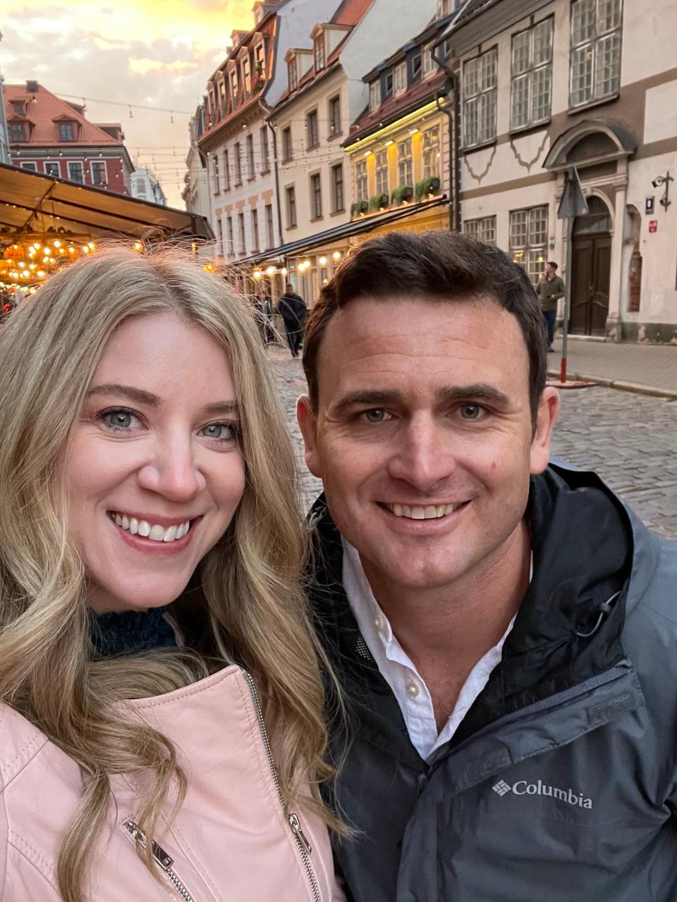 A man and woman take a selfie in front of European buildings.