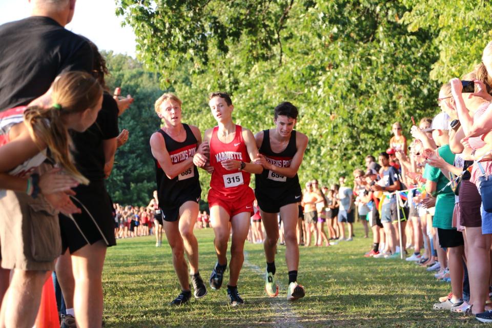 Stevens Point Area High School runners Ethan Olds, left, and Cooper Erickson, right, help Seppi Camilli of Marquette (Michigan) High School after he had fallen neer the finish line in a cross country race Friday in Neenah.