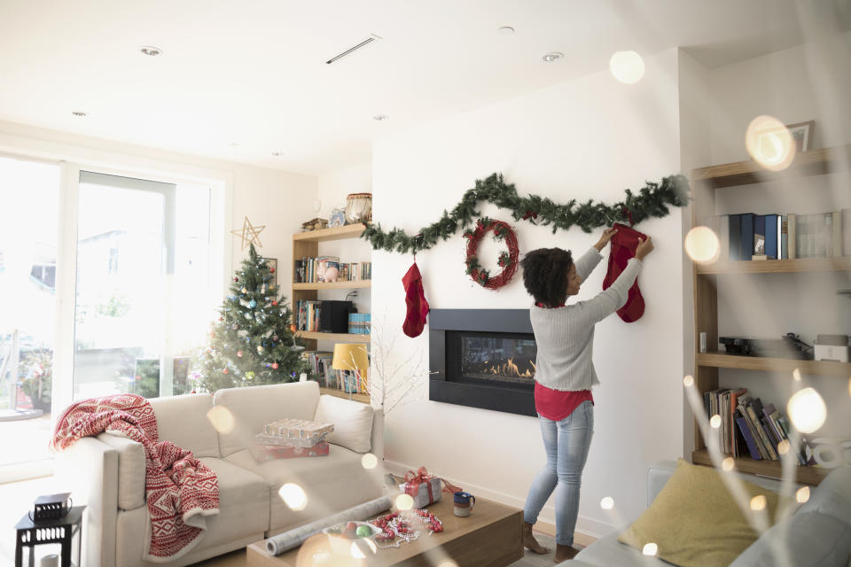 Woman hanging Christmas stocking above fireplace in living room