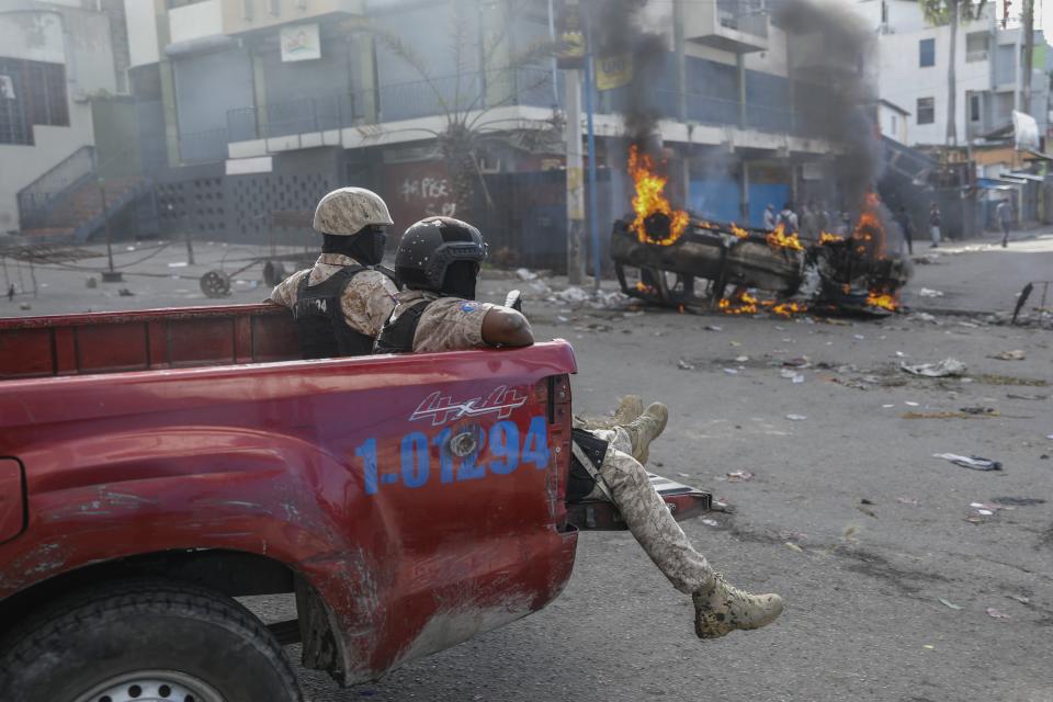 National police officers ride past a vehicle set on fire by protesters during a demonstration demanding the resignation of Prime Minister Ariel Henry, in Port-au-Prince, Haiti, Wednesday, Feb. 7, 2024. (AP Photo/Odelyn Joseph)