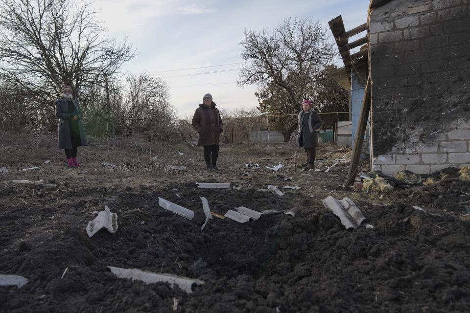 Local residents stand at the scene of an explosion next to their house a damaged house after alleged shelling by separatists forces in Novognativka, eastern Ukraine, Sunday, Feb. 20, 2022. Russia is extending military drills near Ukraine's northern borders after two days of sustained shelling along the contact line between Ukrainian soldiers and Russia-backed separatists in eastern Ukraine. The exercises in Belarus, which borders Ukraine to the north, originally were set to end on Sunday. (AP Photo/Evgeniy Maloletka)