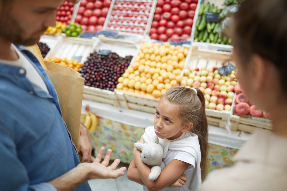 Girl holding a stuffed toy looks up at adults in a grocery store