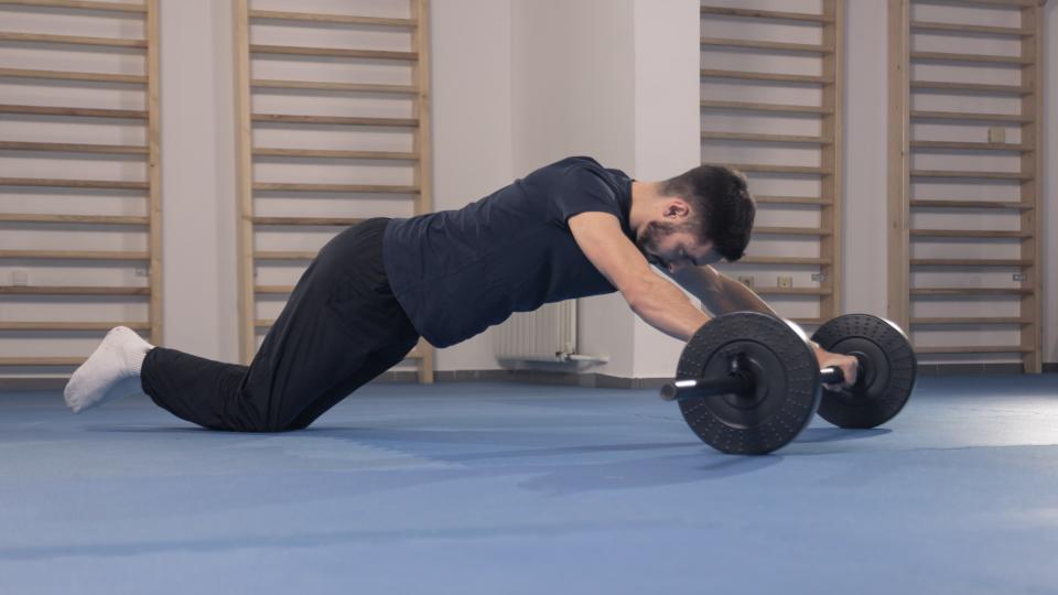 Man performing an ab rollout using a barbell in the gym