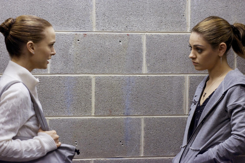 Two women lean against a wall and chat