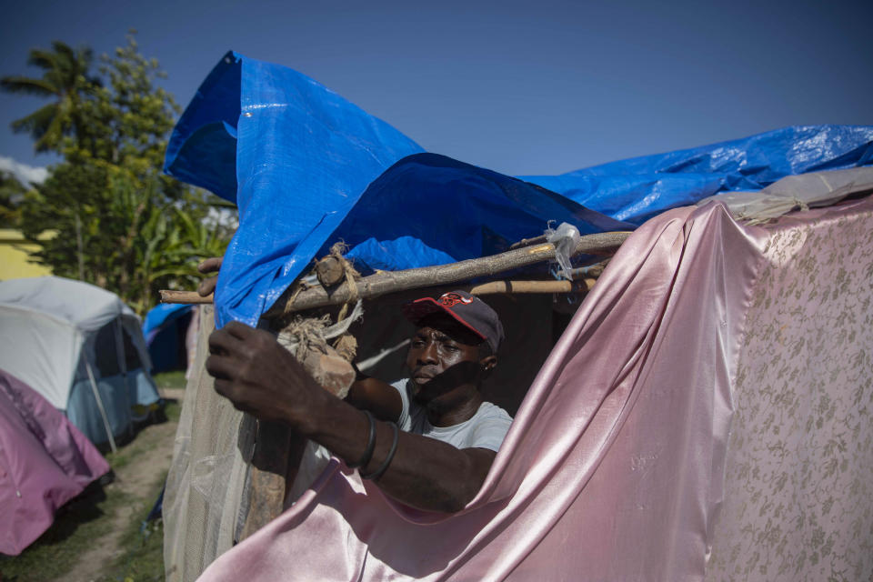 Six months after a 7.2 magnitude earthquake, Guillaume Frenord fixes his makeshift tent at the Devirel camp in Les Cayes, Haiti, Wednesday, Feb. 16, 2022. Thousands of Haitians who lost their homes in the quake remain in camps, living in cramped shelters made of plastic and cloth sheets and corrugated metal. (AP Photo/ Odelyn Joseph)